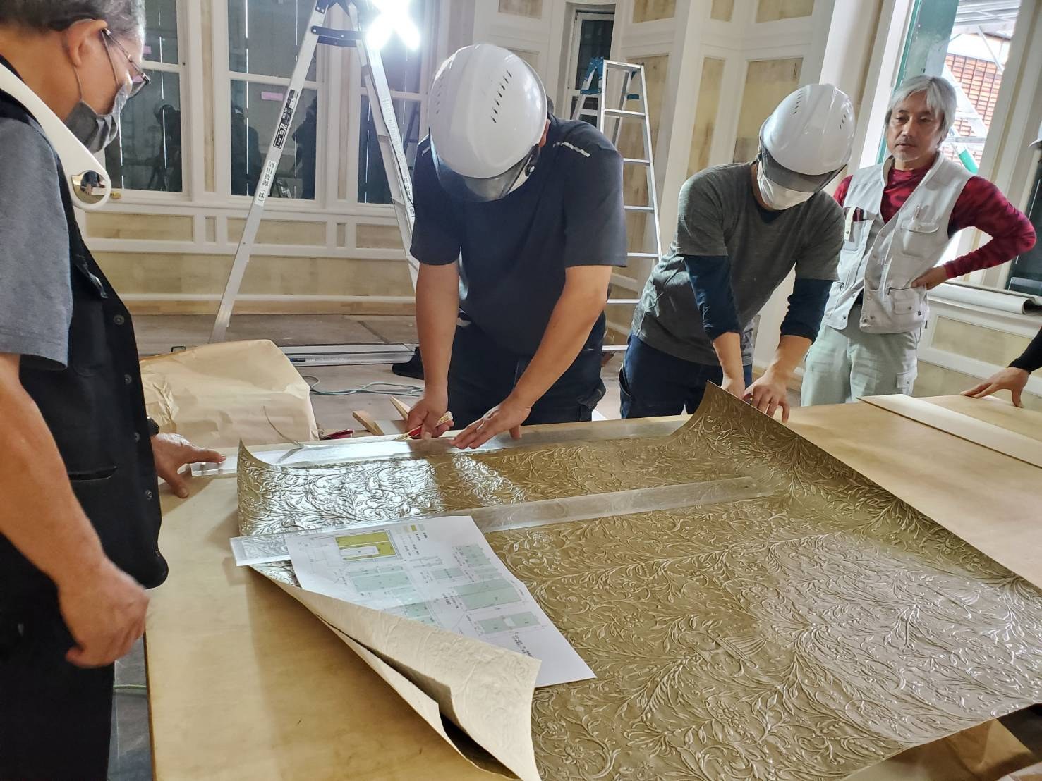 装飾材を扱う職人の手元と、作業を見守る仲間